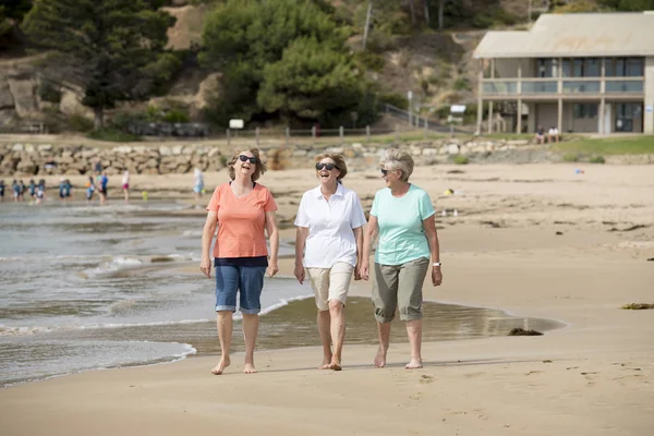 Kelompok yang terdiri dari tiga perempuan dewasa berusia 60-an yang menikmati berjalan-jalan dengan gembira di pantai dengan tersenyum gembira — Stok Foto