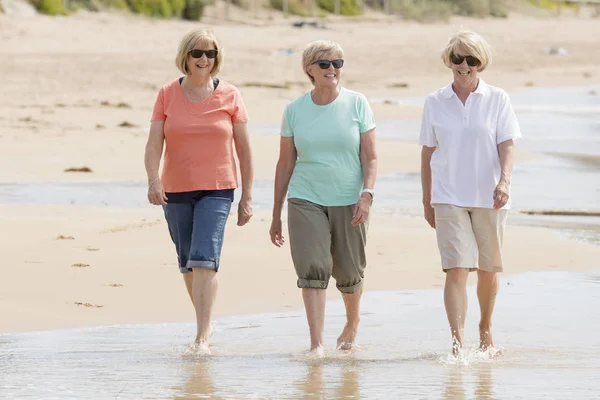 Schöne Gruppe von drei älteren, reifen Rentnerinnen um die 60, die Spaß daran haben, zusammen fröhlich am Strand spazieren zu gehen und dabei verspielt lächelnd — Stockfoto