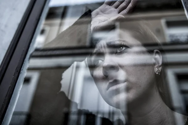 Dramatisches Nahaufnahme-Porträt einer jungen schönen Frau, die traurig ist und Depressionen am Fenster ihres Hauses erleidet und deprimiert wirkt — Stockfoto