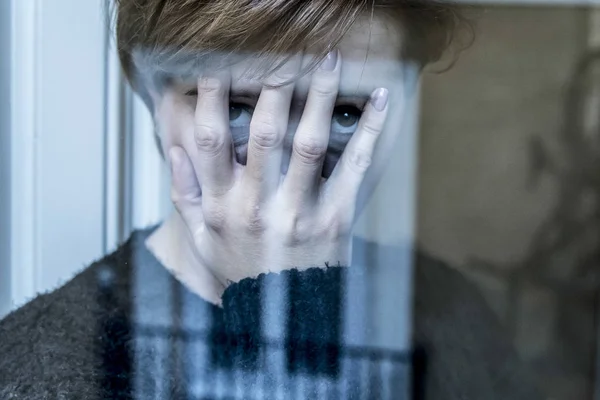 Dramatisches Nahaufnahme-Porträt einer jungen schönen Frau, die traurig ist und Depressionen am Fenster ihres Hauses erleidet und deprimiert wirkt — Stockfoto