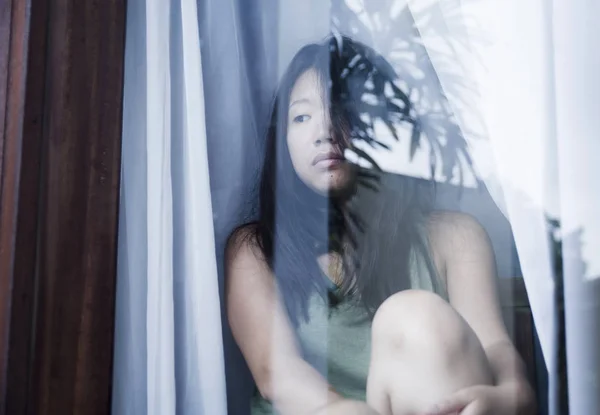Unga ledsen och deprimerad asiatisk kinesisk kvinna ser eftertänksam genom fönsterglas som lider av smärta och depression i sorg koncept — Stockfoto