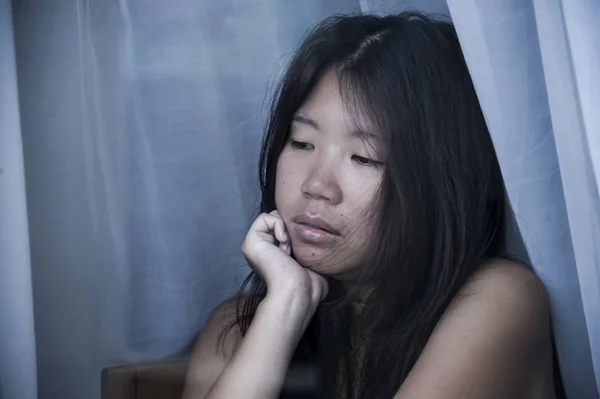 Young sad and depressed Asian Chinese woman looking thoughtful through window glass suffering pain and depression in sadness concept — Stock Photo, Image