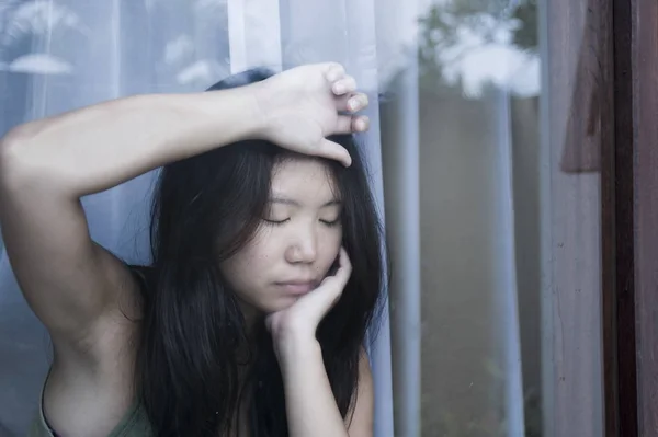 Unga ledsen och deprimerad asiatisk kinesisk kvinna ser eftertänksam genom fönsterglas som lider av smärta och depression i sorg koncept — Stockfoto