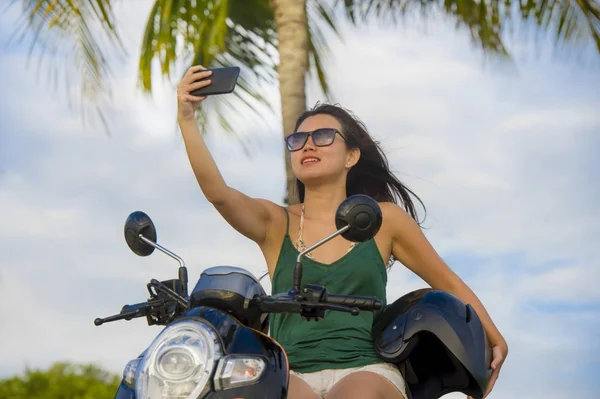 young happy and pretty Asian Chinese woman taking selfie portrait picture with mobile phone camera riding scooter motorbike