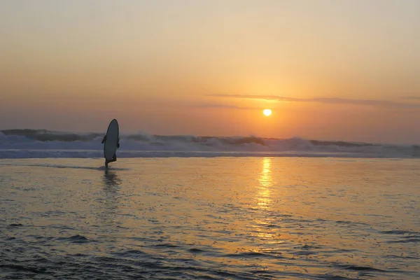 Silhouette eines unbekannten anonymen Surfers mit Surfbrett nach dem Surfen bei Sonnenuntergang mit erstaunlich schönem Sonnenlicht und orangefarbenem Himmel — Stockfoto