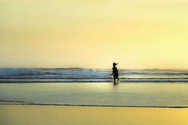 Silhouette d'enfant femelle anonyme courant et jouant sur une magnifique plage désertique au coucher du soleil avec un ciel orange et une lumière dorée — Photo