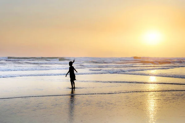 Silhouette of anonymous female child running and playing on amazing beautiful desert beach on sunset with an orange sky and golden light — Stock Photo, Image