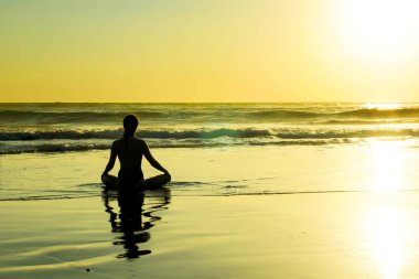 Deniz plaj su pratik yoga ve meditasyon için güneş ufukta seyir üzerinde oturan bilinmeyen tanınmaz halde kadın silüeti