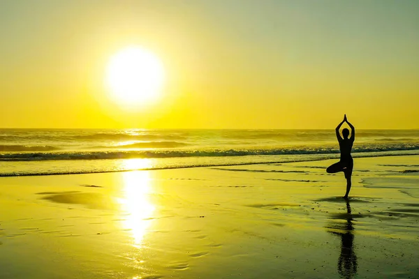 不知名的女人的剪影站立在海滩海水实践瑜伽和凝思看在地平线上的太阳 — 图库照片