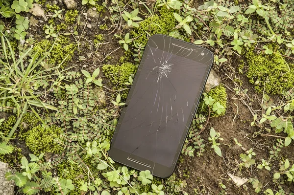 Dispositivo de telefone móvel riscado e quebrado tela de toque rachadura abandonada no chão grama rua em reparação e corrigir o conceito de serviço de telefone inteligente — Fotografia de Stock