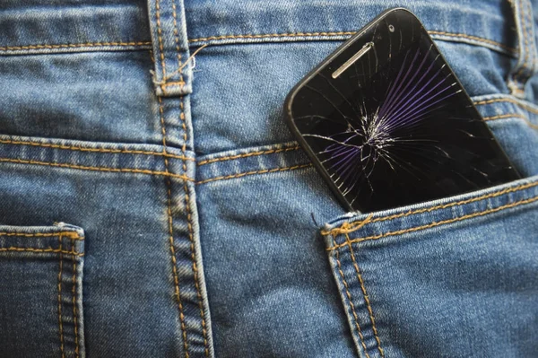 Мобільний телефон зламаний і тріснутий сенсорний екран в задній кишені джинсових джинсових штанів в аварії і недбалої концепції — стокове фото