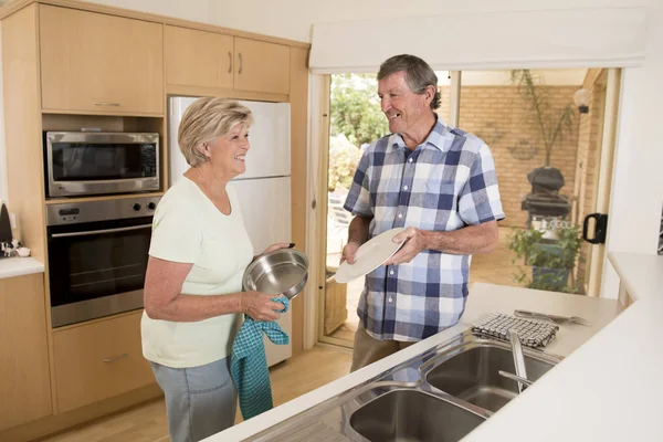 Vedoucí krásnou středního věku kolem 70 let věku s úsměvem šťastný v latexu řetězcích doma kuchyni mytí nádobí hledá sladký dohromady — Stock fotografie