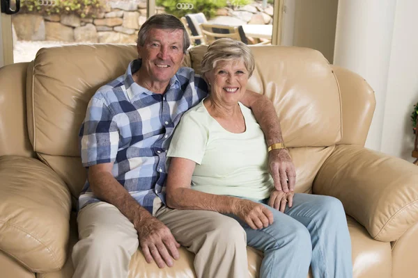 Pasangan usia pertengahan yang cantik sekitar 70 tahun tersenyum bahagia bersama-sama di sofa ruang keluarga tampak manis dalam cinta seumur hidup — Stok Foto