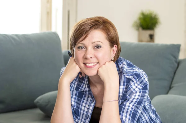 Jonge aantrekkelijke en gelukkig rood haar vrouw ongeveer 30 jaar oud glimlachend zeker thuis woonkamer bedrijf pen in haar hand op zoek ontspannen — Stockfoto