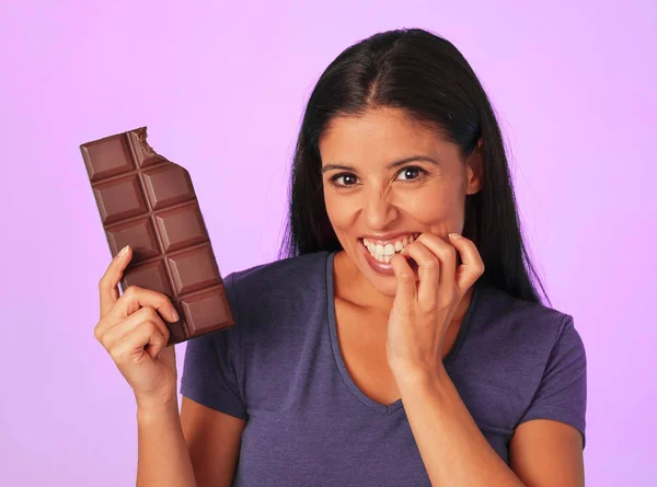 Joven mujer hispana bonita y feliz sosteniendo barra de chocolate con mordedura de dientes sonriendo en azúcar y dulce concepto de adicción — Foto de Stock