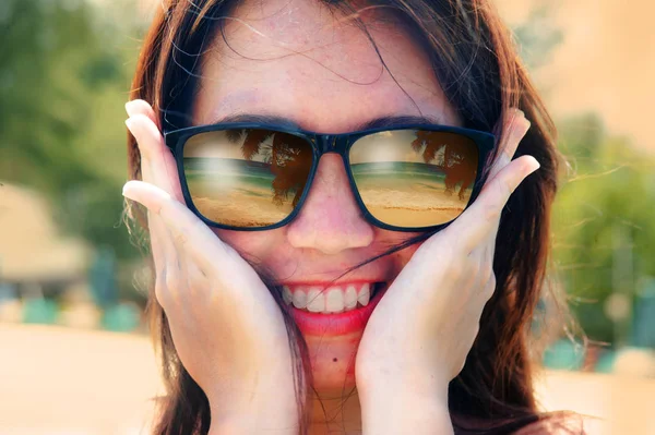Hermosa y feliz mujer asiática sonriendo sosteniendo su cara usando gafas de sol con playa tropical mar y palmera reflexión sobre las gafas en concepto de vacaciones —  Fotos de Stock
