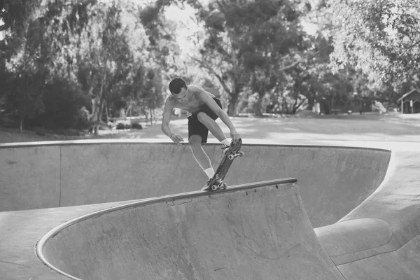 Joven estadounidense en torso desnudo practicando skate board radical saltando y disfrutando de trucos y acrobacias en pista de patinaje de medio tubo de hormigón — Foto de Stock