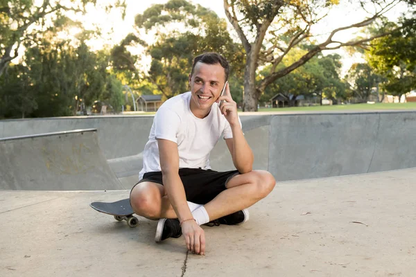 Mutlu ve çekici Amerikalı genç adam cep telefonu üzerinde konuşurken eğitim oturumu yatılı spor sonra paten kurulu üzerinde oturan 30'lu — Stok fotoğraf