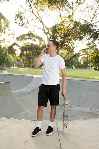 Jovem feliz e atraente americano 30 anos em pé segurando skate board após esporte embarque sessão de treinamento falando no telefone móvel — Fotografia de Stock