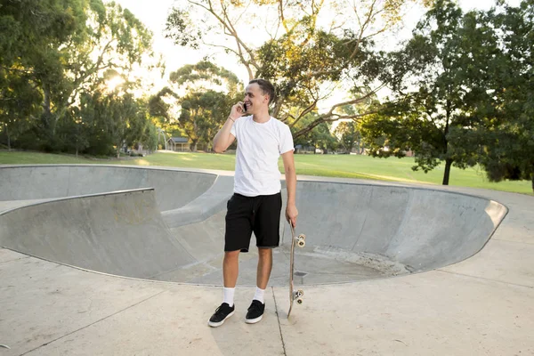 Jovem feliz e atraente americano 30 anos em pé segurando skate board após esporte embarque sessão de treinamento falando no telefone móvel — Fotografia de Stock