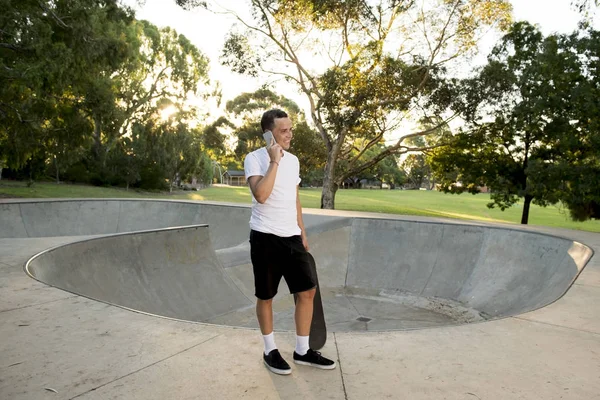 Jovem feliz e atraente americano 30 anos em pé segurando skate board após esporte embarque sessão de treinamento falando no telefone móvel — Fotografia de Stock