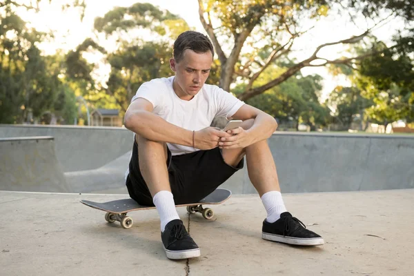 アメリカ スポーツ インターネットのソーシャル メディアのテキストを送信する携帯電話を使用してトレーニングを搭乗後スケート ボードに座っている 30 代の男 — ストック写真