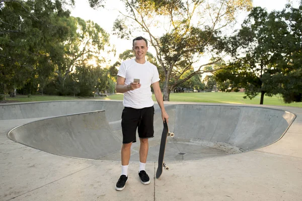 Homem de 30 anos de pé segurando skate board após esporte embarque sessão de treinamento usando telefone celular na faixa de meia tubulação — Fotografia de Stock