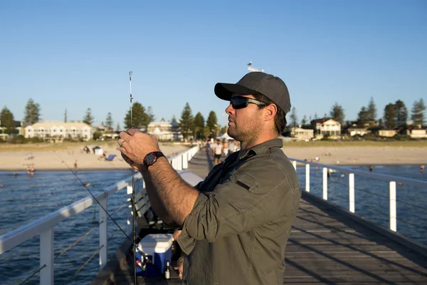 young attractive and happy man in shirt and hat fishing at beach sea dock using fish road enjoying weekend hobby in holidays