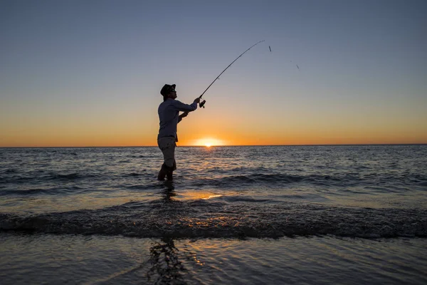 Silhouet van visser met hoed op het strand met vis Rod staande op zee water vissen bij zonsondergang met prachtige oranje hemel in vakanties Rechtenvrije Stockafbeeldingen