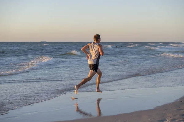 Αθλητική fit και ισχυρή δρομέας άνθρωπος κατάρτισης στο ηλιοβασίλεμα παραλία το καλοκαίρι στη θάλασσα ακτή τρέχει και γυμναστήριο προπόνηση στον αθλητισμό και υγιεινό τρόπο ζωής — Φωτογραφία Αρχείου