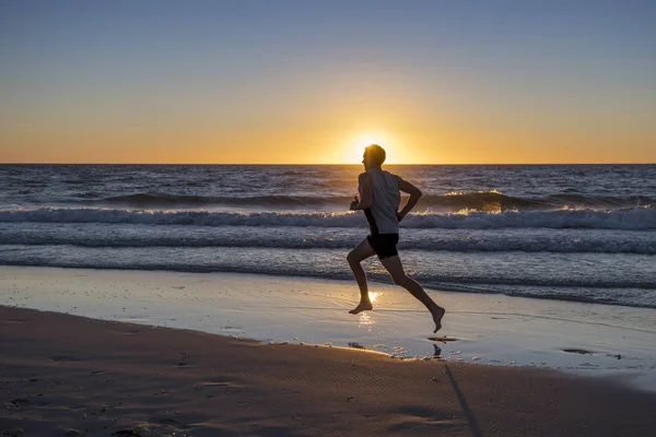 Silhouette jeune athlète dynamique coureur homme avec fit forte musculation sur été coucher de soleil plage course pieds nus dans le sport sain et concept de fitness — Photo