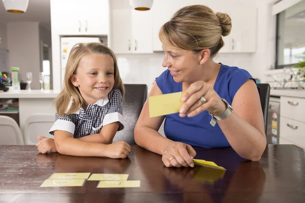 Feliz jovem mãe e sua doce e bela filhinha jogando jogo de cartas em casa cozinha sorrindo e se divertindo juntos — Fotografia de Stock