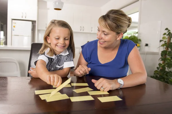 Feliz jovem mãe e sua doce e bela filhinha jogando jogo de cartas em casa cozinha sorrindo e se divertindo juntos — Fotografia de Stock