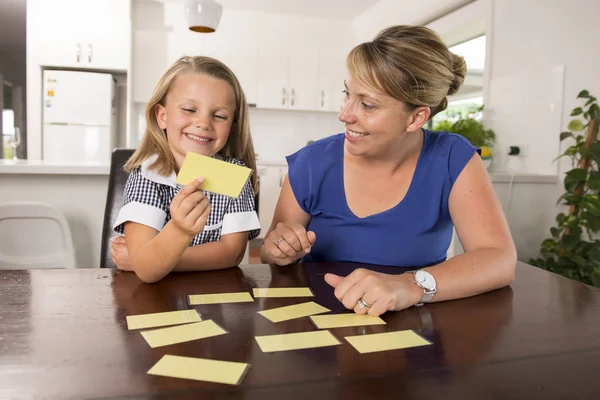 Feliz jovem mãe e sua doce e bela filhinha jogando jogo de cartas em casa cozinha sorrindo e se divertindo juntos — Fotografia de Stock