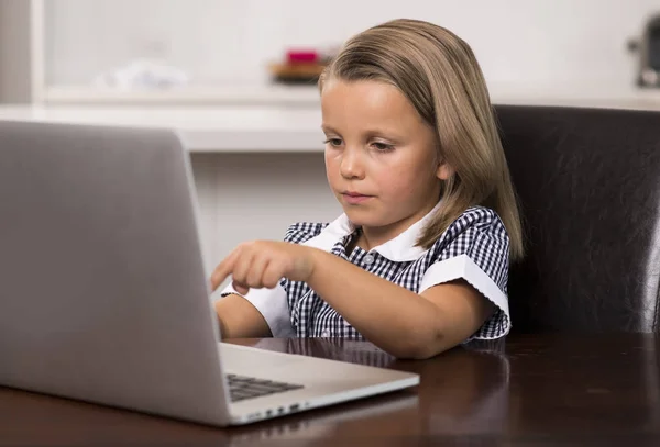 Маленькая девочка от 6 до 8 лет сидит на домашней кухне наслаждаясь ноутбуком сконцентрированы смотреть интернет мультфильм — стоковое фото