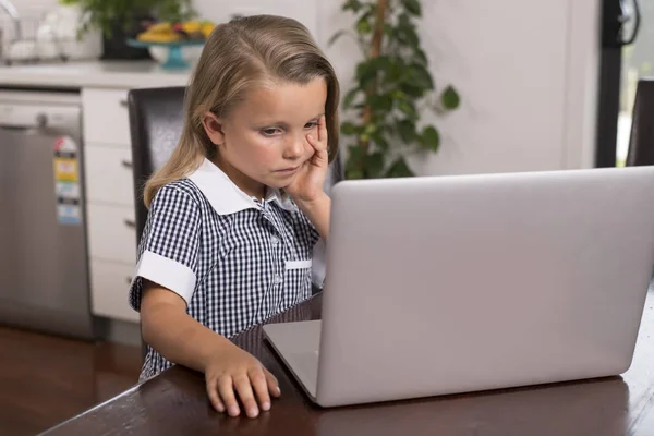 Niña de 6 a 8 años de edad sentado en casa cocina disfrutando con el ordenador portátil concentrado viendo películas de dibujos animados de Internet — Foto de Stock