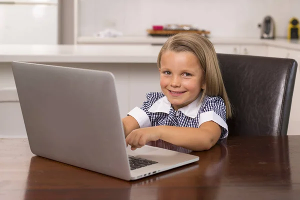 Jovem menina bonita e doce 6 a 8 anos com cabelo loiro e olhos azuis sentados em casa cozinha desfrutando com computador portátil sorrindo feliz — Fotografia de Stock