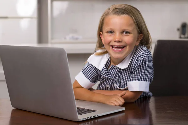 Jovem menina bonita e doce 6 a 8 anos com cabelo loiro e olhos azuis sentados em casa cozinha desfrutando com computador portátil sorrindo feliz — Fotografia de Stock