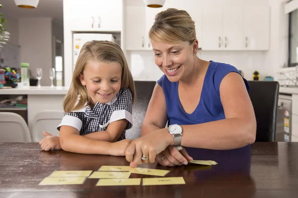 Lovely sweet and happy 6 years old daughter learning reading with flash card words game at home kitchen playing with her young beautiful mother — Stock Photo, Image