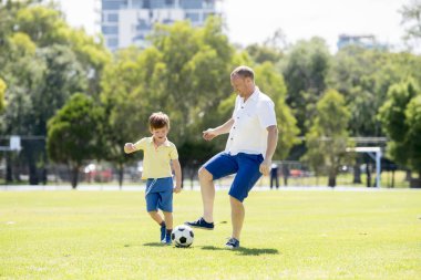 Genç mutlu baba ve heyecanlı küçük 7 ya da 8 yaşında oğlu birlikte şehir park Bahçe topu tekmeleme çimenlerin üzerinde çalışan futbol futbol oynama