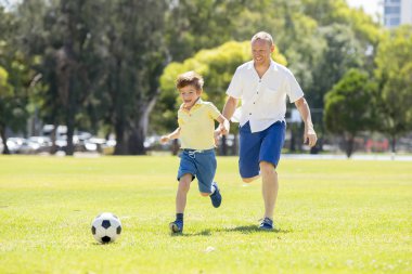 Genç mutlu baba ve heyecanlı küçük 7 ya da 8 yaşında oğlu birlikte şehir park Bahçe topu tekmeleme çimenlerin üzerinde çalışan futbol futbol oynama