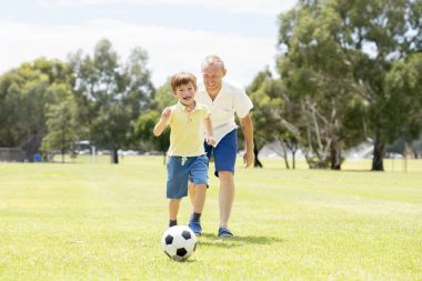 Genç mutlu baba ve heyecanlı küçük 7 ya da 8 yaşında oğlu birlikte şehir park Bahçe topu tekmeleme çimenlerin üzerinde çalışan futbol futbol oynama