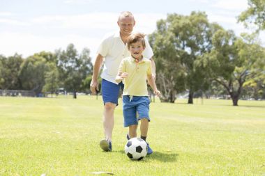 Genç mutlu baba ve heyecanlı küçük 7 ya da 8 yaşında oğlu birlikte şehir park Bahçe topu tekmeleme çimenlerin üzerinde çalışan futbol futbol oynama