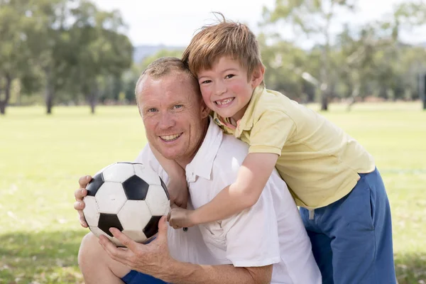 young happy father and excited 7 or 8 years old son playing together soccer football on city park garden posing sweet and loving holding the ball
