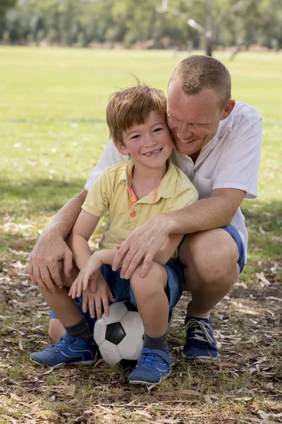 Genç mutlu baba ve heyecanlı 7 ya da 8 yaşında oğlu birlikte futbol futbol topu tutan sevgi dolu ve tatlı poz şehir park Bahçe üzerinde oynama — Stok fotoğraf