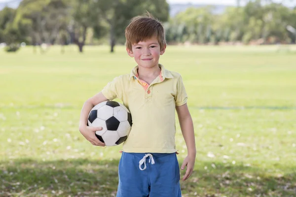 Jovem criança 7 ou 8 anos de idade desfrutando de futebol feliz jogando futebol no campo do parque da cidade grama posando sorrindo orgulhoso de pé segurando a bola — Fotografia de Stock