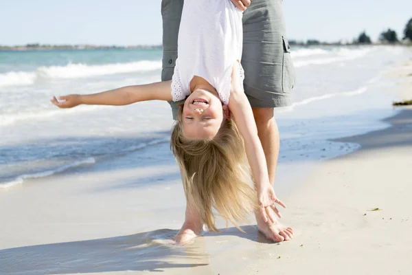 Pai segurando doce jovem e adorável loira pequena filha por seus pés brincando se divertindo na praia em pai e conceito de amor menina — Fotografia de Stock