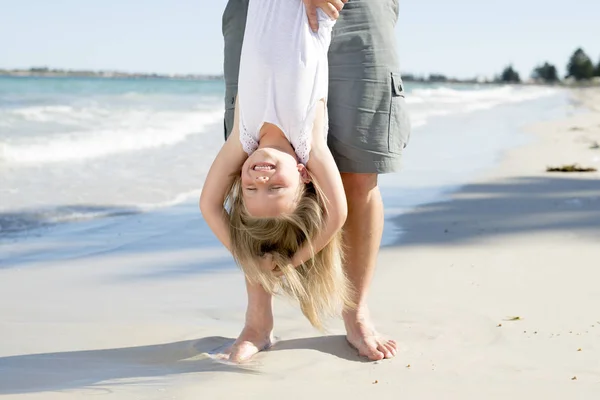 Pai segurando doce jovem e adorável loira pequena filha por seus pés brincando se divertindo na praia em pai e conceito de amor menina — Fotografia de Stock