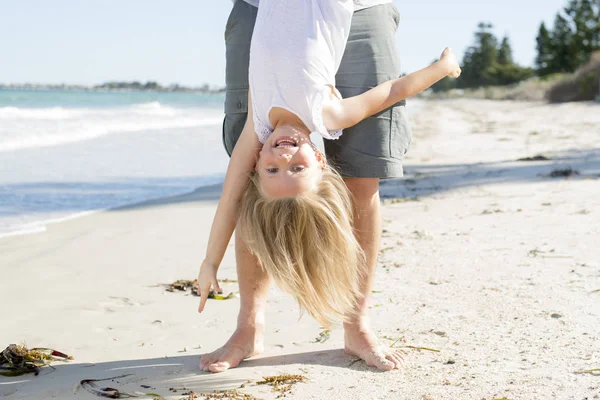 Pai segurando doce jovem e adorável loira pequena filha por seus pés brincando se divertindo na praia em pai e conceito de amor menina — Fotografia de Stock