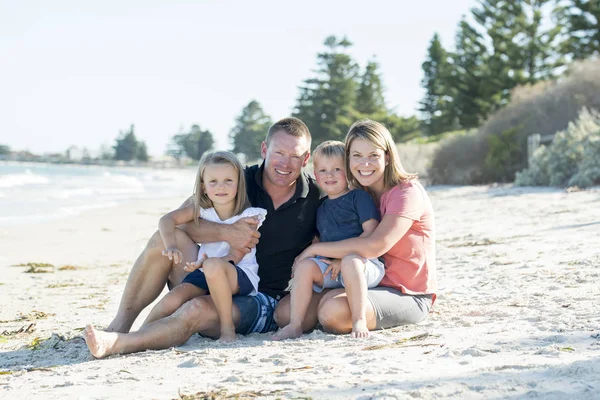 Glada vackra kaukasiska familjen ha semester på stranden leende med mor och far sitter på sand med lilla son och ung dotter — Stockfoto